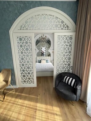 A bedroom with a bed, a chair, a sofa, and a decorative arched doorway. - Rikhe Palace Boutique HOTEL (Tbilisi)