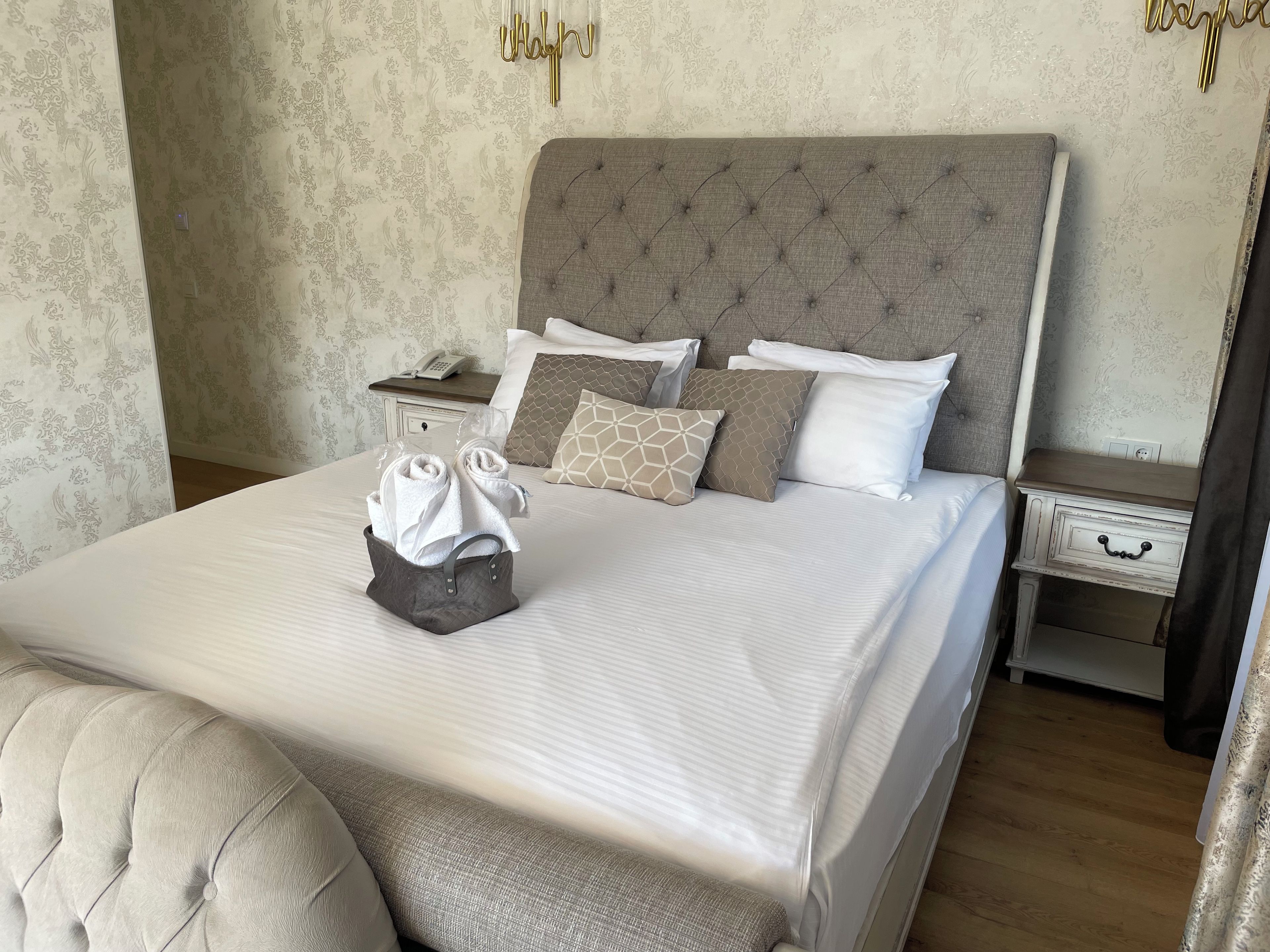 Un lit bien fait, avec une tête de lit grise, une table de chevet sur laquelle se trouve un téléphone, et un mur orné d’un motif floral.