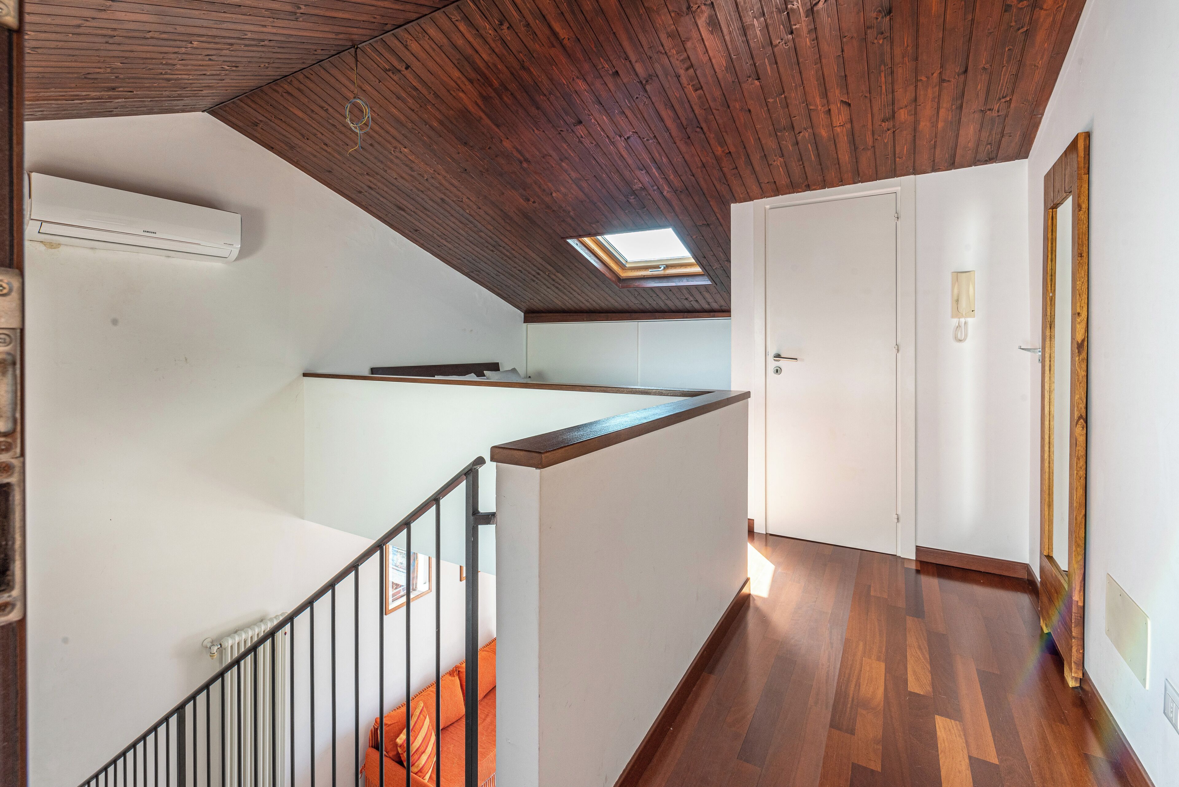 Un interior de varios niveles con techo de madera, tragaluz, puerta blanca y suelo de madera.