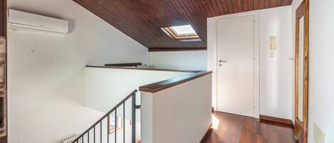 Un interior de varios niveles con techo de madera, tragaluz, puerta blanca y suelo de madera.