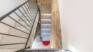 Eine Treppe mit Metallgeländer, Steinwänden und einem roten Teppich am Fuß.