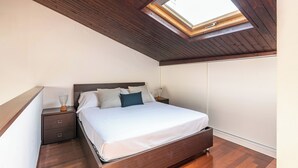 Ein Schlafzimmer mit Oberlicht, Holzboden und einem Bett mit weißer Bettwäsche, einem Nachttisch und einer Kommode.