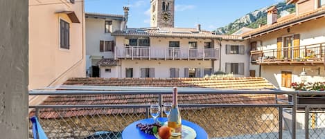 Un balcón con una mesa para dos personas, que incluye una botella y copas, con vista a un edificio con una torre de reloj.