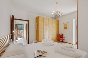 A hotel room with a bed, a chandelier, a wardrobe, and a red chair. - Kirribilli House (Nago-Torbole)