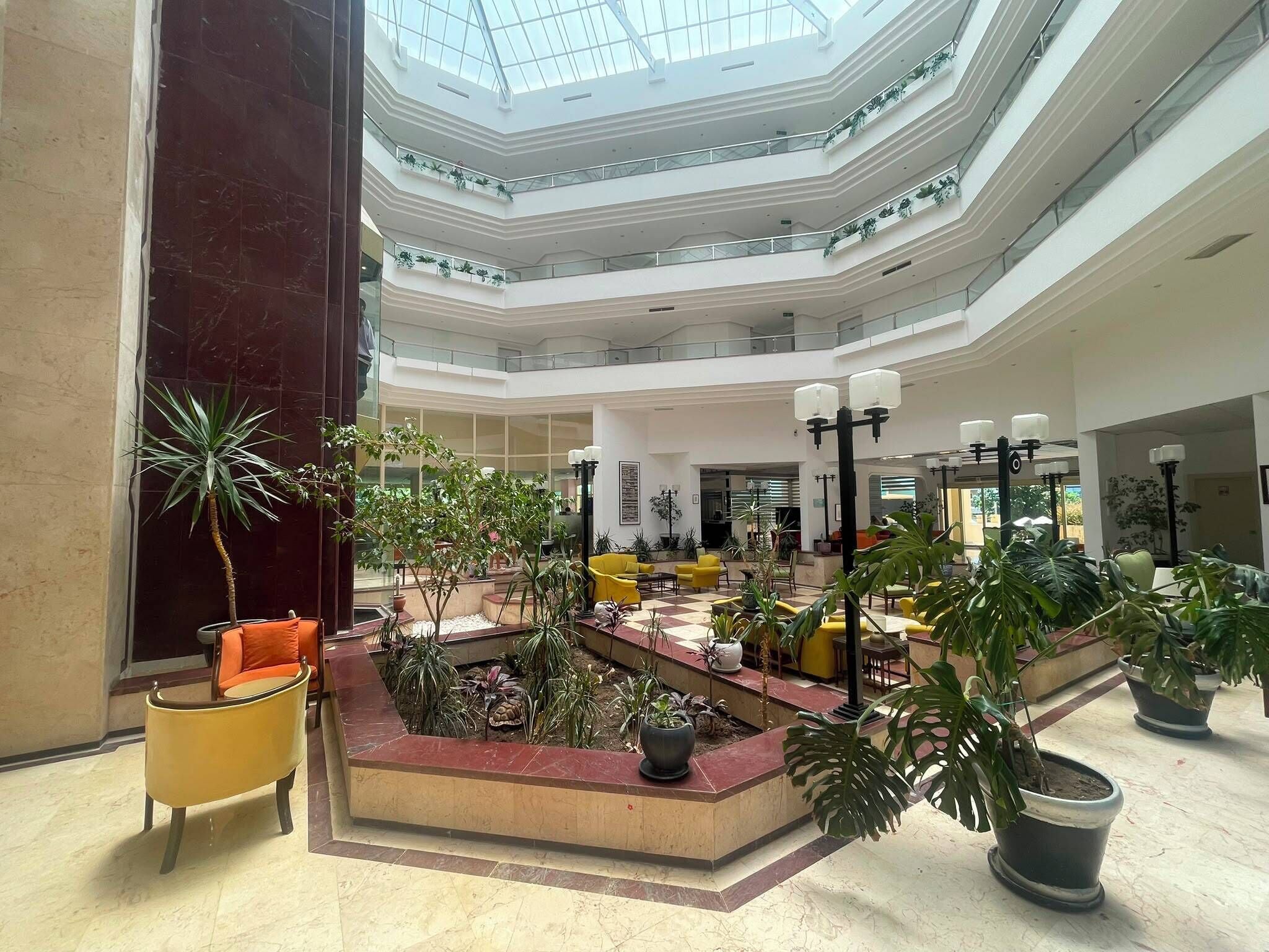 Un atrio de varios niveles con un jardín central, zonas de estar y un techo de cristal.