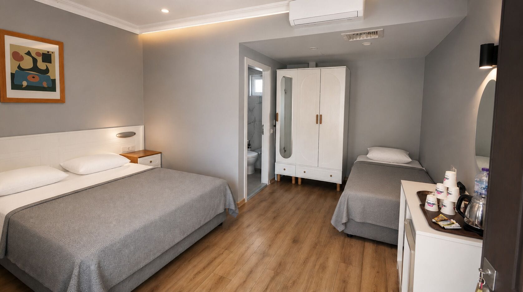 Una habitación de hotel con dos camas, un armario, un espejo y una mesita de noche con una lámpara.