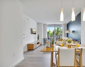 A modern dining area with a wooden table, white chairs, and pendant lights. - Grand 1BR · Intracoastal & Sunset View · Resort (Hallandale Beach)