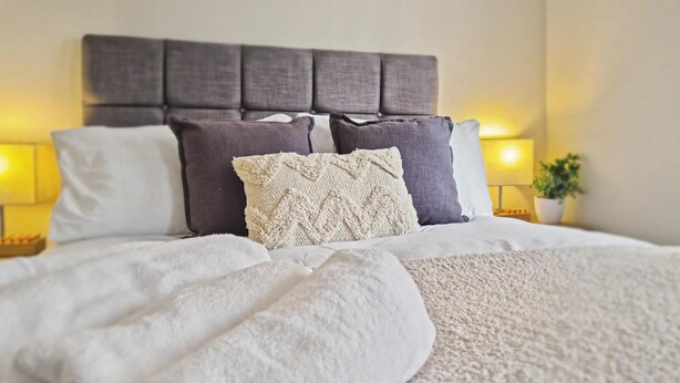 A neatly made bed with a grey upholstered headboard, white and grey pillows, and a white throw blanket. - Stylish 2BR Solihull Stay | Near NEC | Parking | Garden (Solihull)