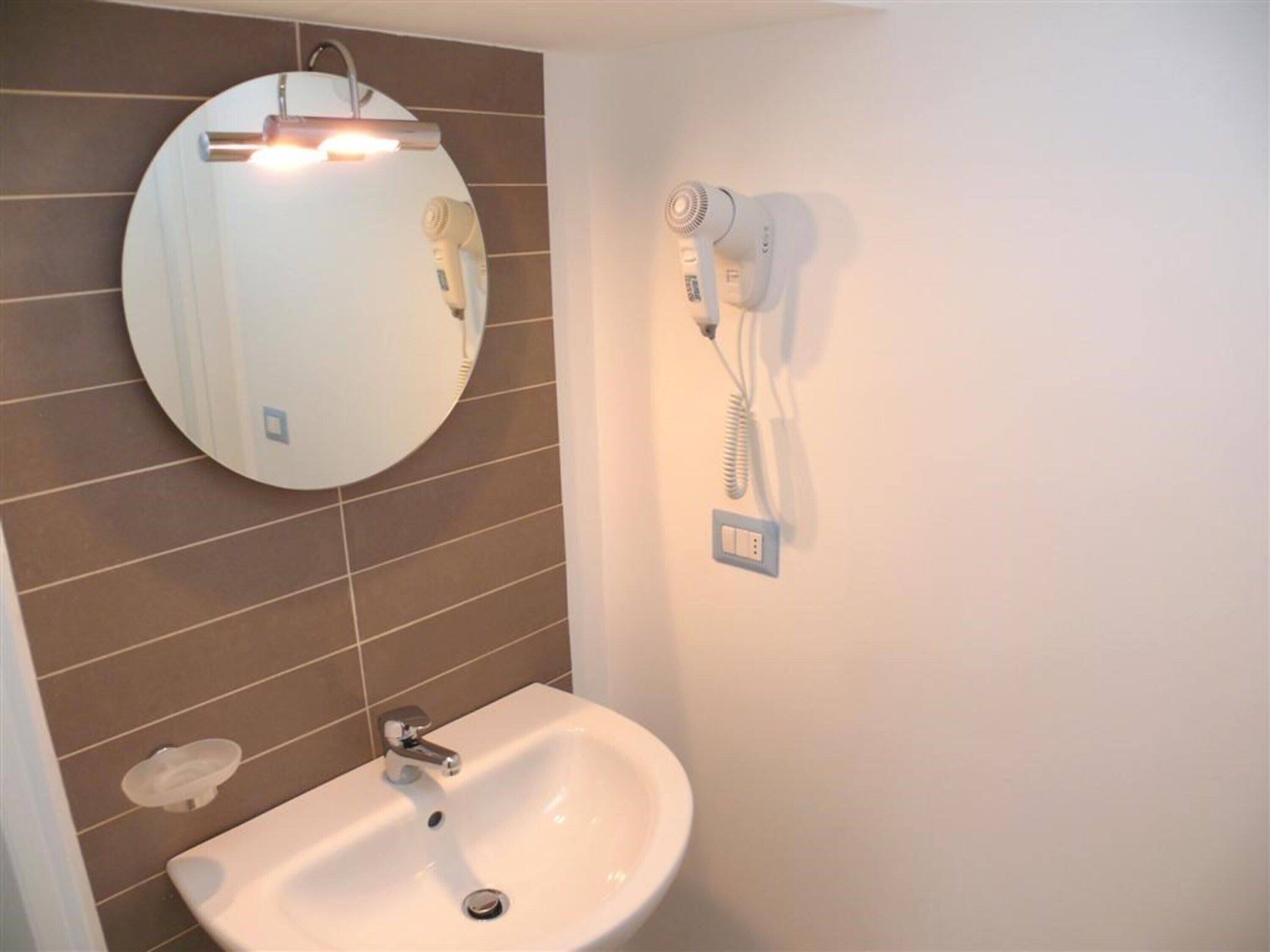 A bathroom with a sink, mirror, and hairdryer mounted on the wall.