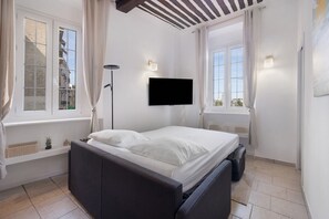 Een slaapkamer met een bed, een aan de muur bevestigde televisie en een raam met gordijnen.