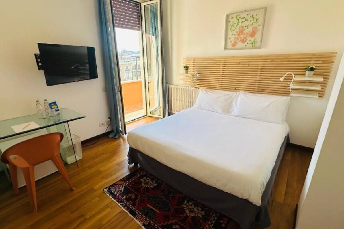 A hotel room with a bed, a desk with a chair, a television, and a window with a view.