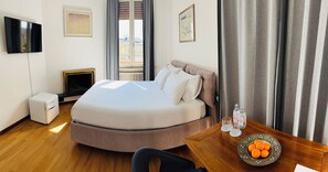 Habitación de hotel con cama, televisión, una mesita con botellas de agua, frutero y ventana con cortinas.