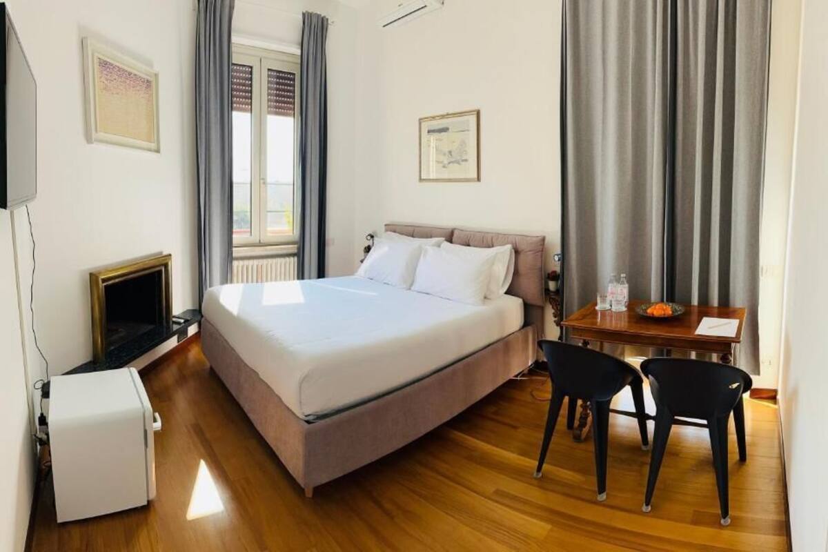 A hotel room with a bed, a desk with chairs, a television, and a radiator.