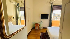A hotel room with a bed, a desk, a chair, a TV, and a window with a view of buildings. - Terrazza Urania (Rome)