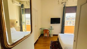 A hotel room with a bed, a desk, a chair, a TV, and a window with a view of buildings. - Terrazza Urania (Rome)