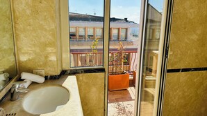 A bathroom with a bathtub, a toilet, a sink, and a window with a view of a building and a balcony. - Terrazza Urania (Rome)