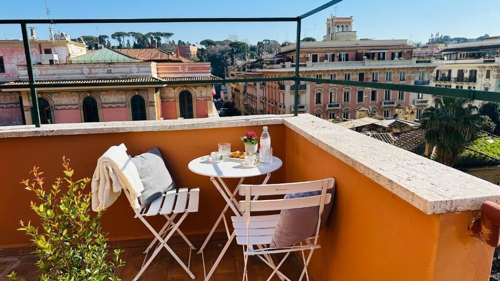 Un balcón con una mesa y sillas, una planta pequeña y vistas a edificios históricos.