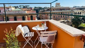 Un balcón con una mesa y sillas, una planta pequeña y vistas a edificios históricos.