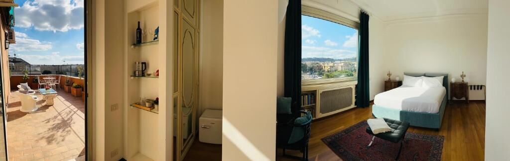 Quarto com janela ampla, cama, mesa de cabeceira e vista da cidade.