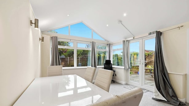 A room with a large white table, two chairs, a black bag, and a view of a garden through large windows. - Charming house with Garden in Aylesbury (Aylesbury)