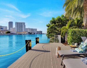 A waterfront balcony with lounge chairs, a pool, and a city skyline in the background. - Stunning Waterway View · 2BR Resort Suite (Hallandale Beach)
