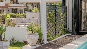 Et poolområde med en hvid pergola, udendørs møbler og krukker med planter.