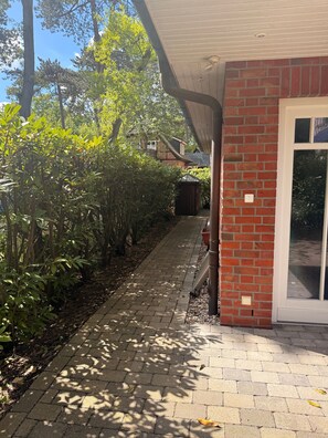 Ein Weg führt zu einem Gebäude mit einer Ziegel Fassade und einer Tür mit Fensterteil.
