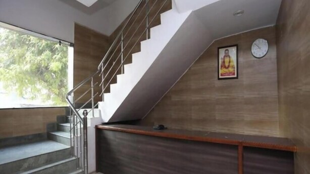 Una escalera con barandilla metálica, un mostrador de recepción con detalles en madera oscura y un reloj en la pared.