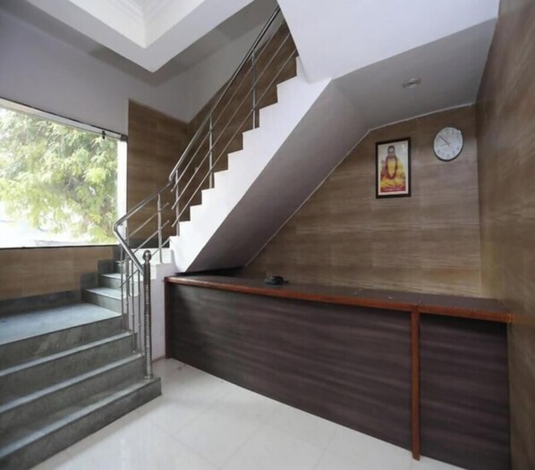 A staircase with a metal railing, a reception desk with a dark wood finish, and a clock on the wall.