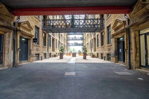 Ein offener Innenhof mit überdachtem Gang, umgeben von Backsteingebäuden mit 'WAREHOUSE'-Schildern und Blumentöpfen.