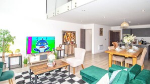 A modern living room with a flat-screen TV, a dining area, and a kitchen in the background. - Charming 2-bedroom Apartment in Bradford With City Views (Bradford)