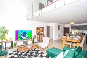 Ein modernes Wohnzimmer mit Fernseher, Essbereich und einer Küche im Hintergrund.
