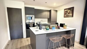A modern kitchen with a built-in oven, microwave, and sink, a small island with bar stools, and a painting on the wall. - Charming 2-bedroom Apartment in Bradford With City Views (Bradford)