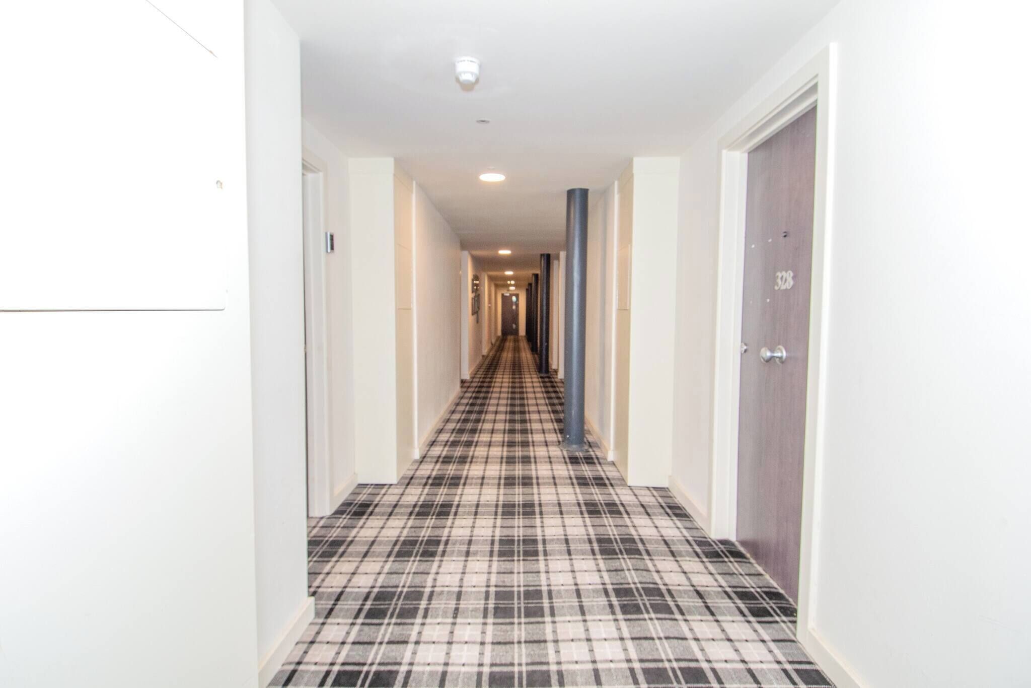 Un pasillo de hotel con piso a cuadros, paredes blancas y puertas a ambos lados.