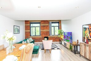 Ein modernes Wohnzimmer mit einer Wand in Holzoptik, einem grünen Sofa, einem Esstisch mit weißen Tellern und einem Fernseher.