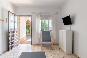 Ein Zimmer mit einem Sessel, einem Fernseher, einer Tür und einem Fenster.