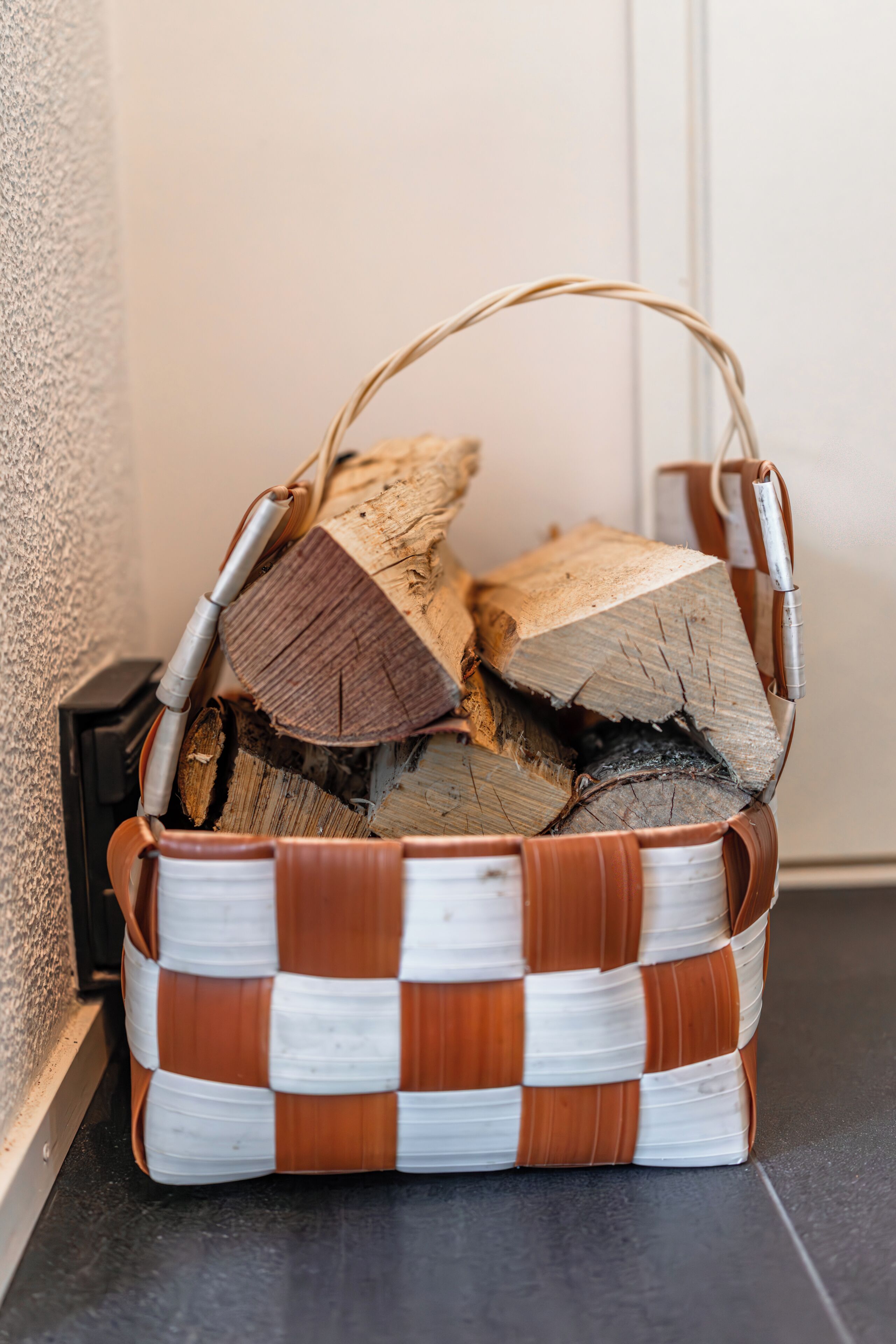 A woven basket with a handle, containing a stack of firewood.