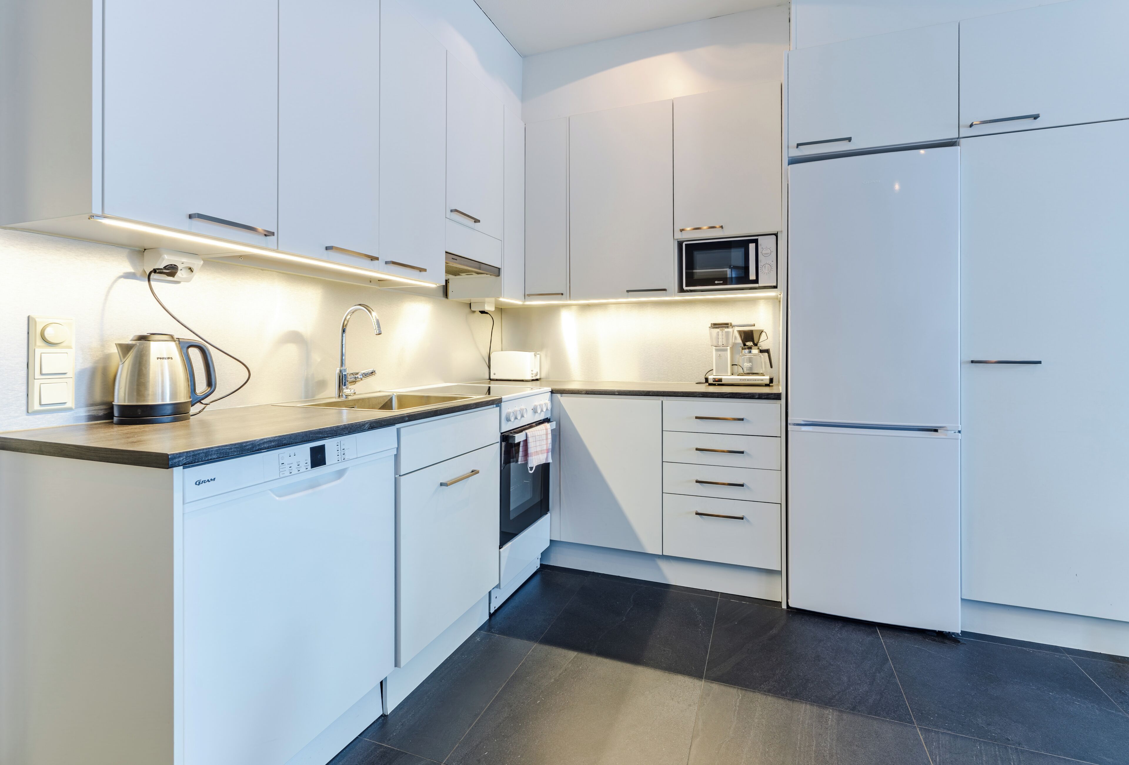 A modern kitchen with white cabinetry, a built-in microwave, a coffee maker, and a dishwasher.