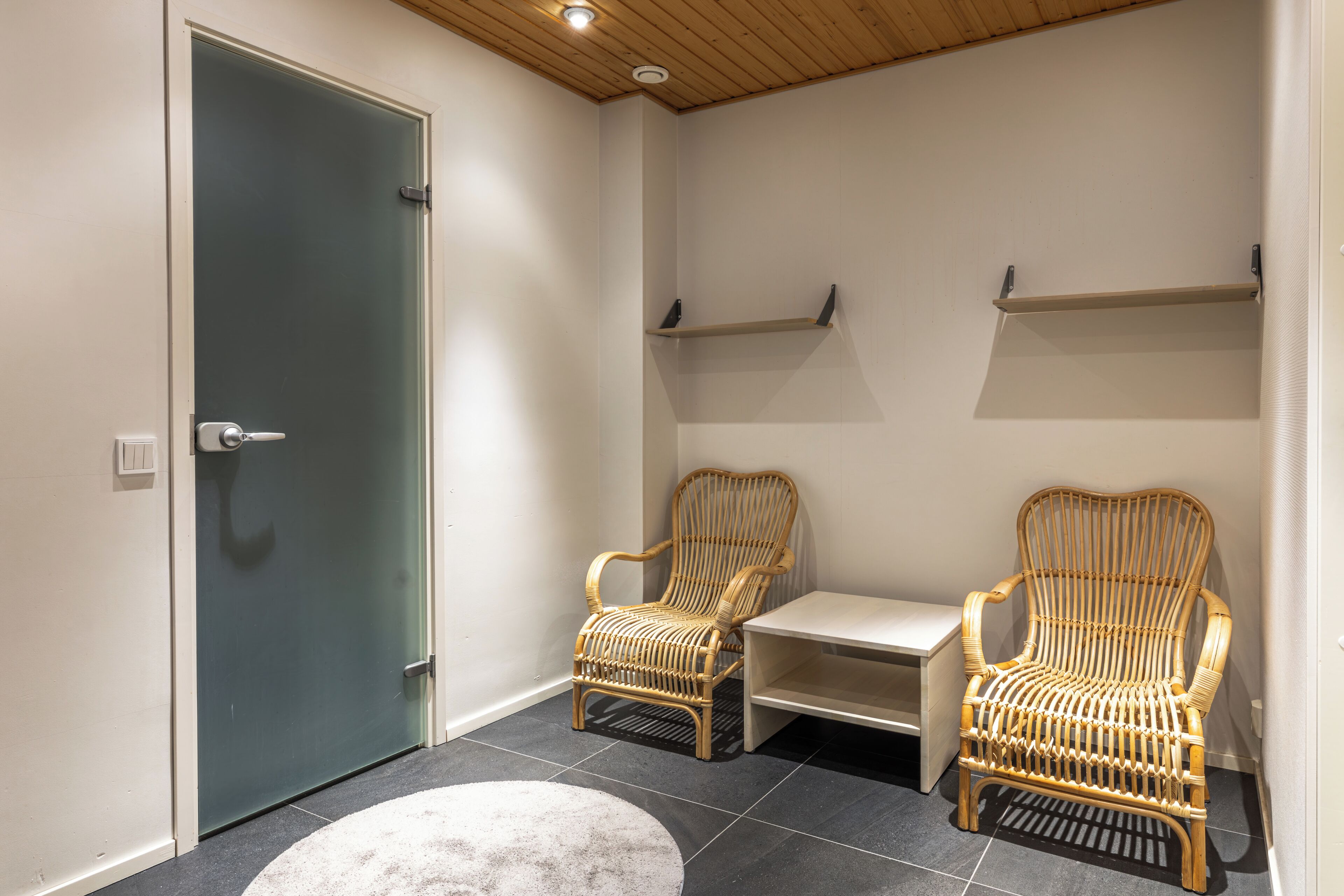 Una habitación con dos sillones de mimbre, una mesita y una puerta.