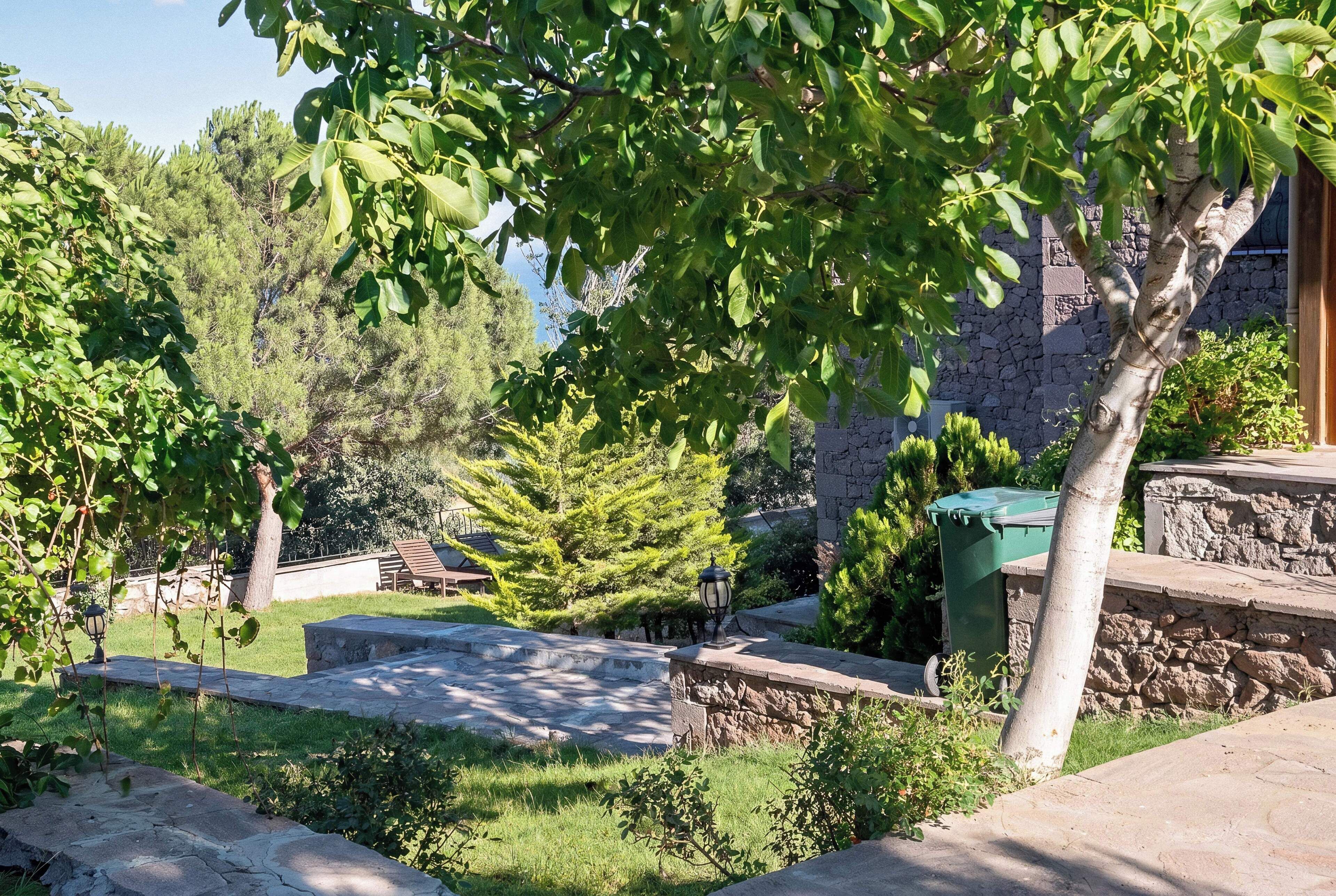 Un chemin de pierres menant à un mur de pierres, avec une poubelle verte et un lampadaire.
