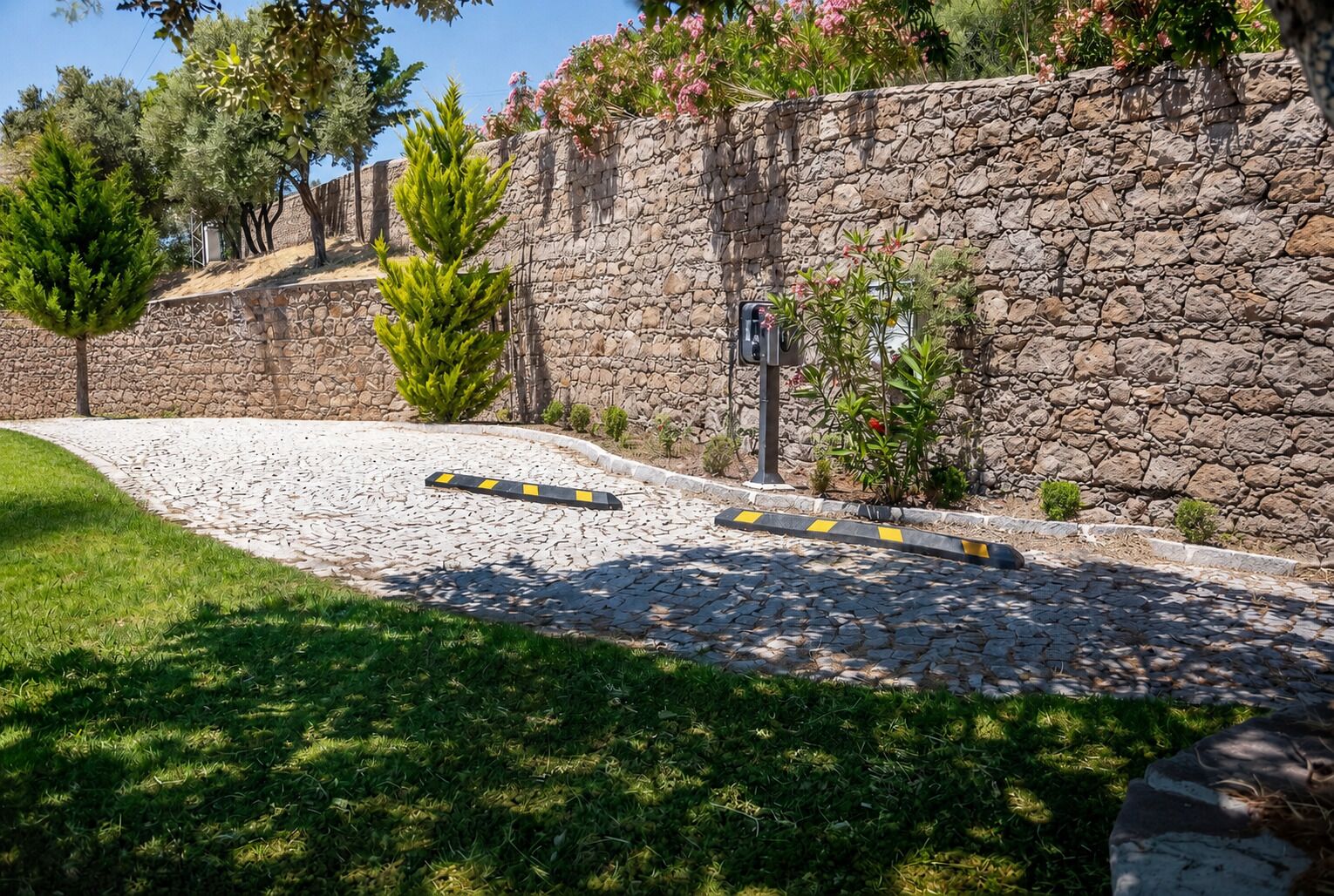 A stone wall with a paved path, greenery, and a bollard.