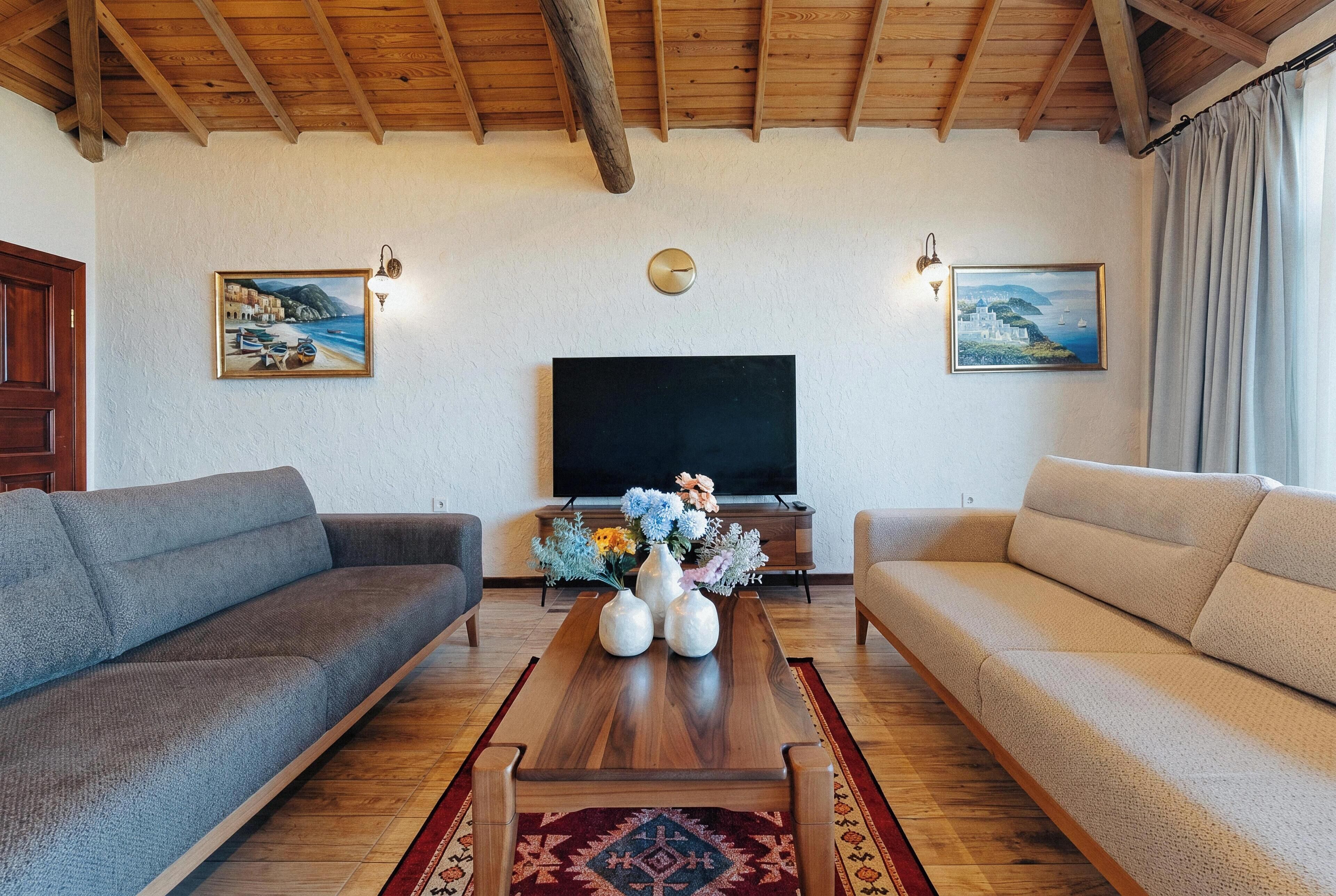 A living room with two sofas, a coffee table with vases, a TV, and paintings on the wall.