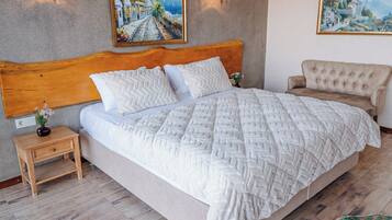 Un dormitorio con cabecera de madera, una cama grande con edredón blanco texturizado, dos lámparas fijadas a la pared y dos cuadros enmarcados.