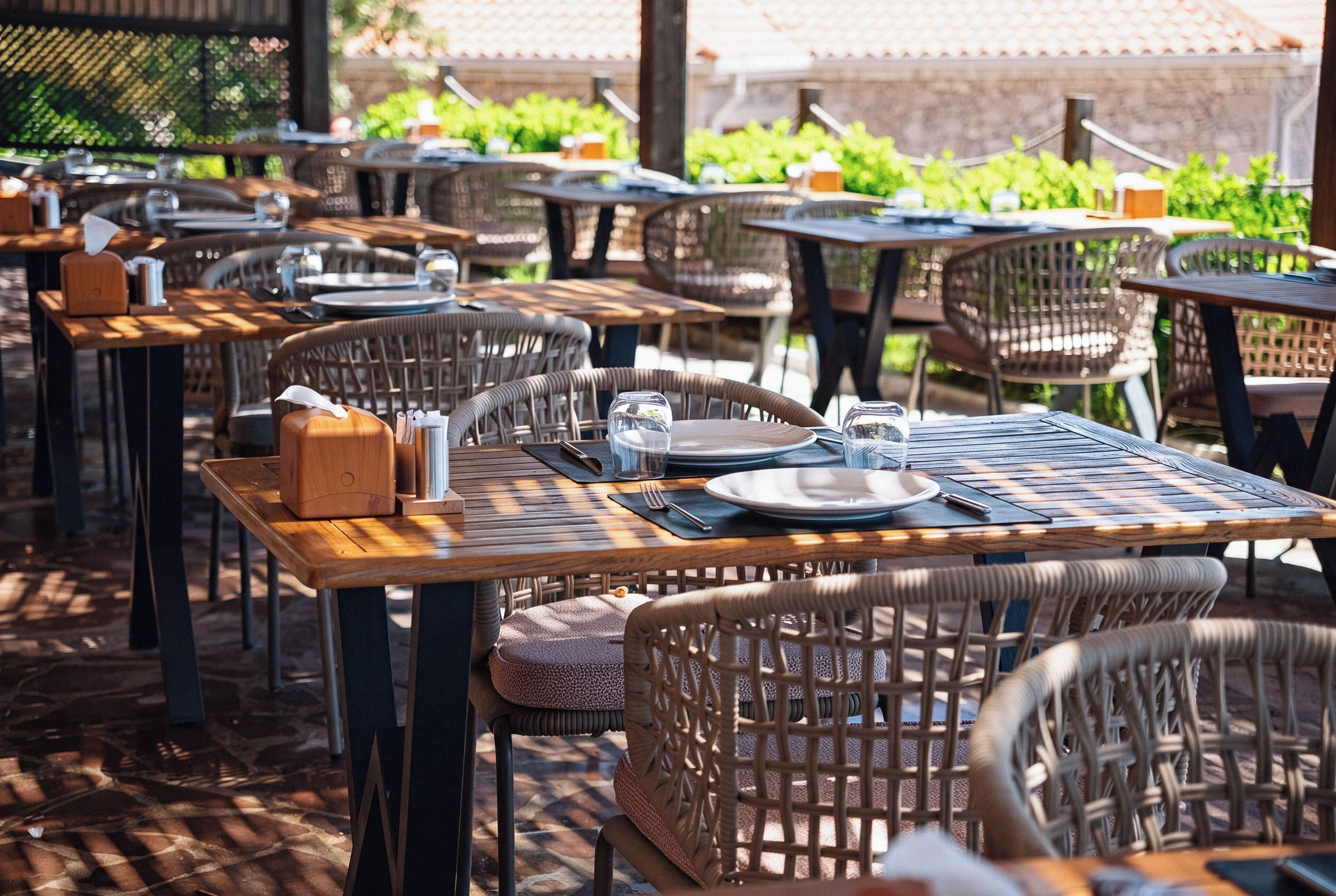 An outdoor dining area with wicker chairs and tables, some with napkins and condiments.