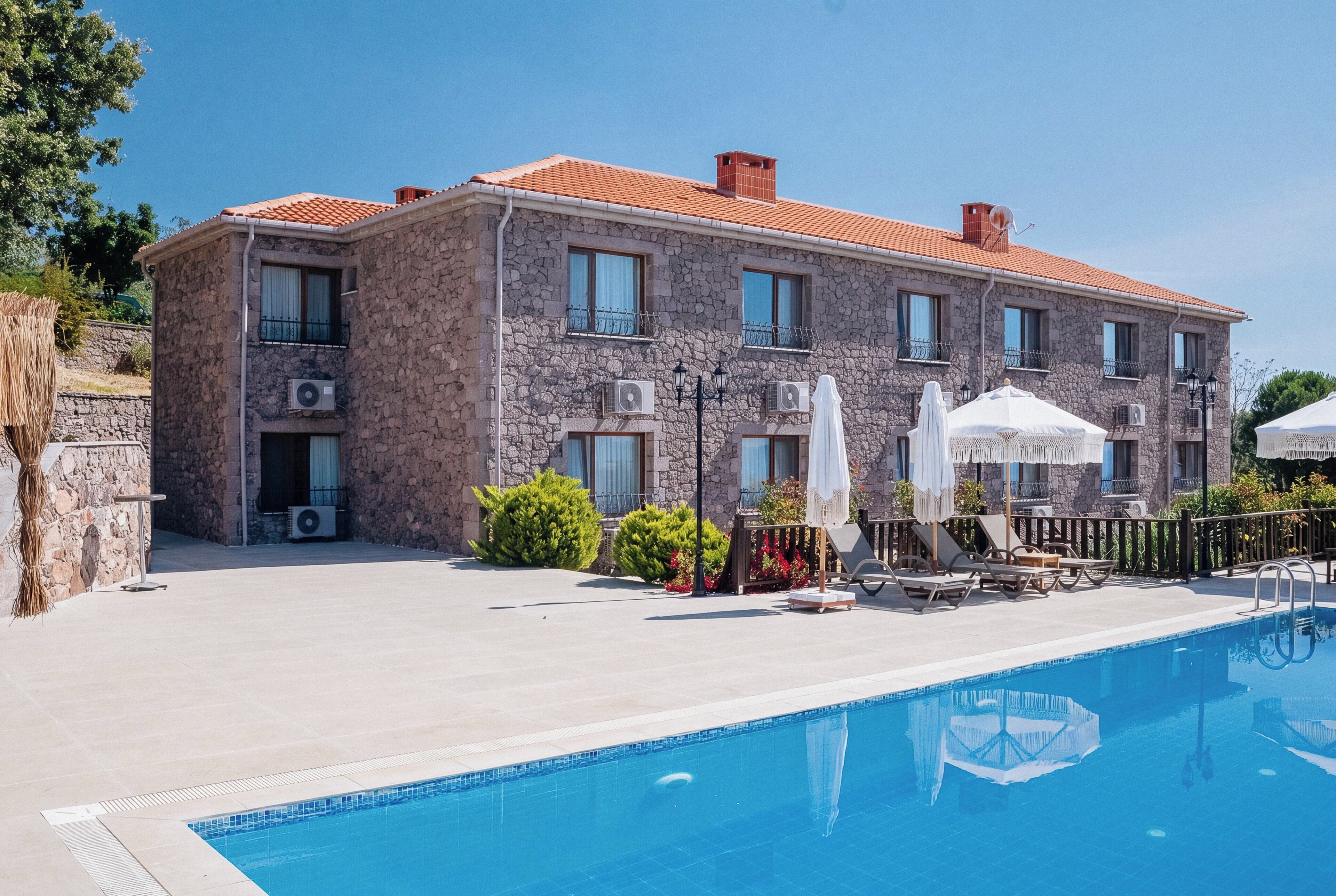 A stone building with a swimming pool, outdoor seating, and umbrellas.
