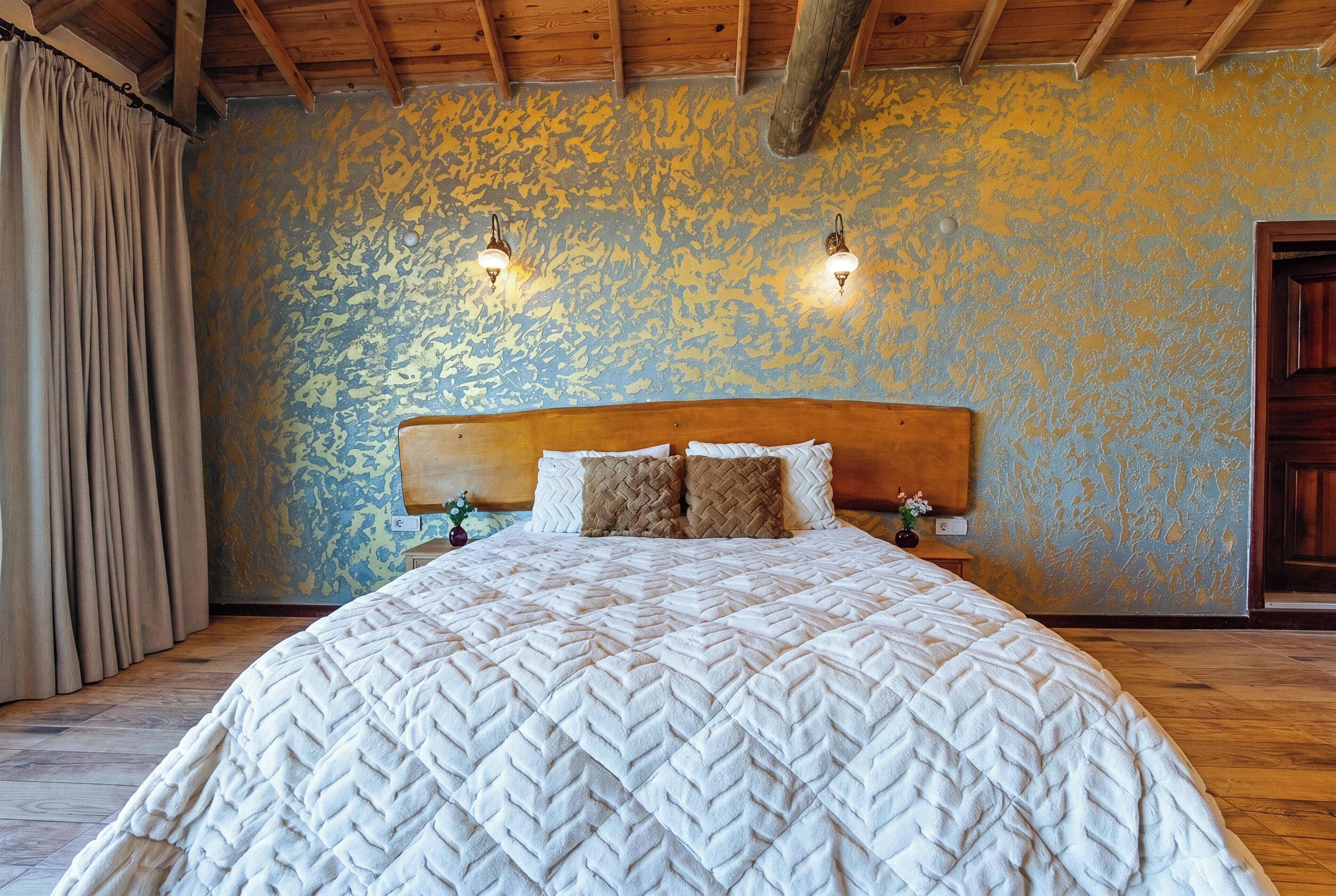 A bed with a quilted blanket, two wall-mounted lamps, and a wooden headboard.