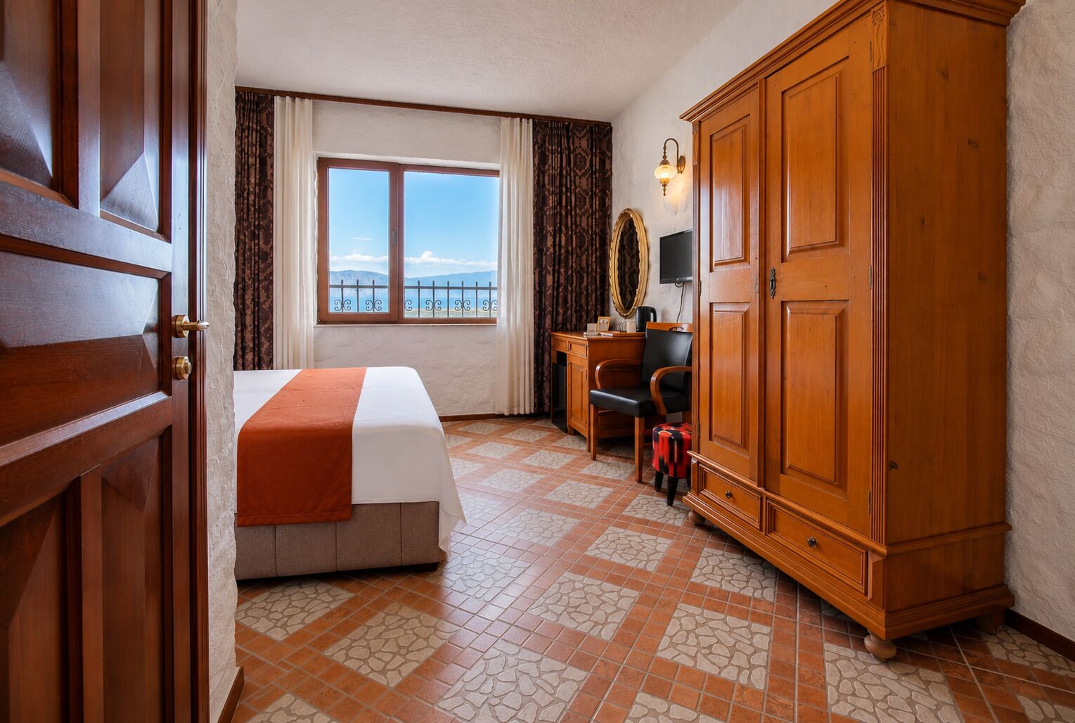 Une chambre d’hôtel comprenant un lit, un bureau, une armoire, une fenêtre avec vue et un sol carrelé.