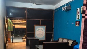 A modern living room with a sofa, a coffee table, and a TV. There is a ceiling fan and a window with blinds. - Amrit Hotel & Resort (Thanagazi)
