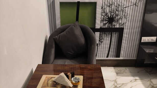 A modern living room with a dark wooden coffee table, a grey sofa, and a striped wall with a green accent. - Amrit Hotel & Resort (Thanagazi)