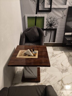 A modern living room with a dark wooden coffee table, a grey sofa, and a striped wall with a green accent. - Amrit Hotel & Resort (Thanagazi)